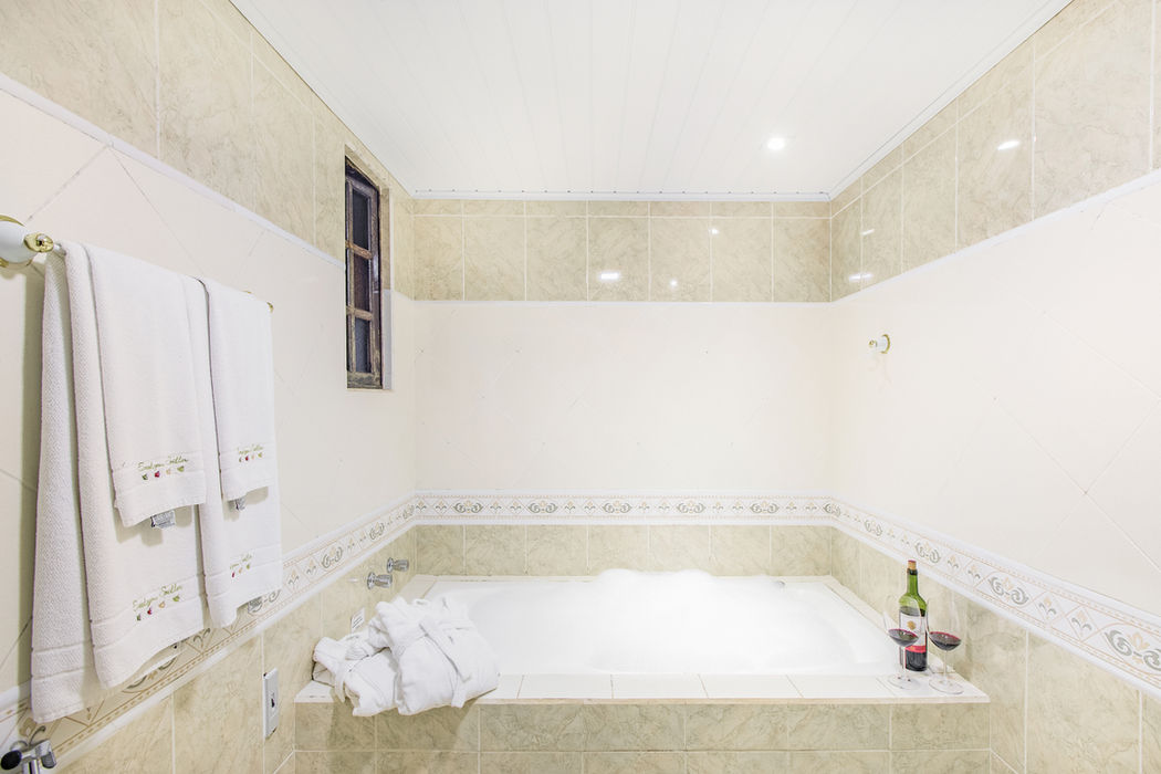 Banheira de hidromassagem na Estalagem Spiller com azulejos em tons de bege, faixa decorativa, janela estreita, barra de toalhas dourada com toalhas brancas em Monte Verde