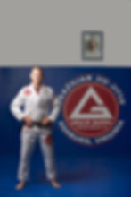 Professor James from the Gracie Barra Ashburn Jiu-Jitsu academy, a man with a shaved head and short beard, is wearing a white gi with red details and a black jiu-jitsu belt, smiling at the camera inside the academy in Virginia.
