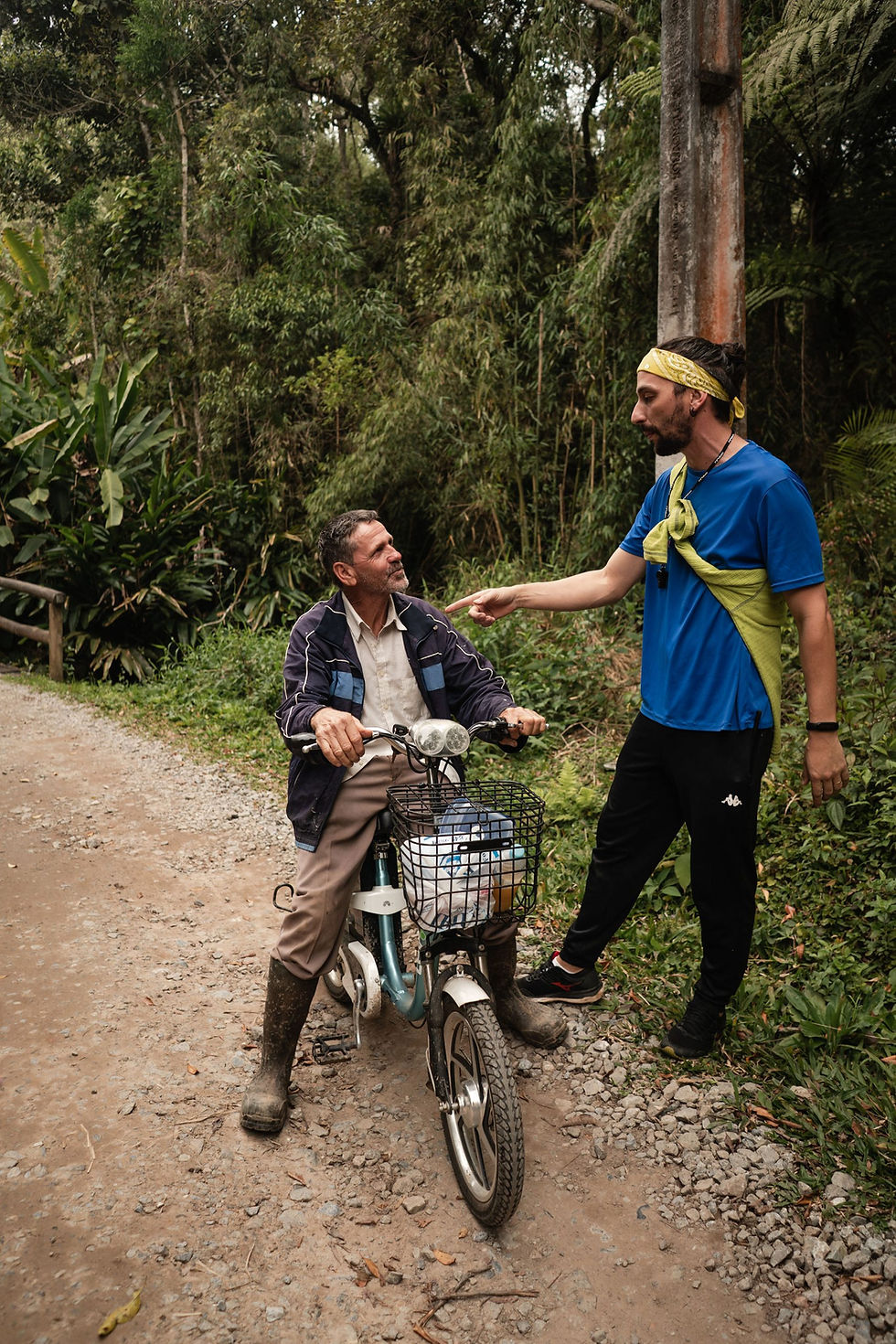 Two men, one standing and the other sitting on a motorcycle, talking on a dirt trail at the Hotel Fazenda Morros Verdes Ecolodge in Ibiúna SP