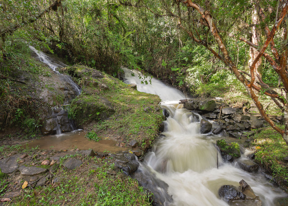 Vista da cachoeira privativa, com pedras, queda d'água e vegetação, na Pousada Cachoeira da Barra em Cunha