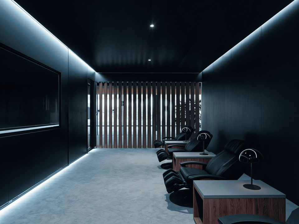 A dark and modern room with three black leather recliner chairs, each with a light wooden side table and a small lamp, at Trein Club in Houston