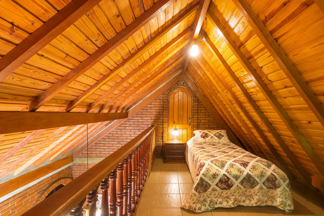 Chalé em mezanino com teto e paredes de madeira, cama de solteiro florida, abajur e porta arqueada com grade na Estalagem Spiller em Monte Verde