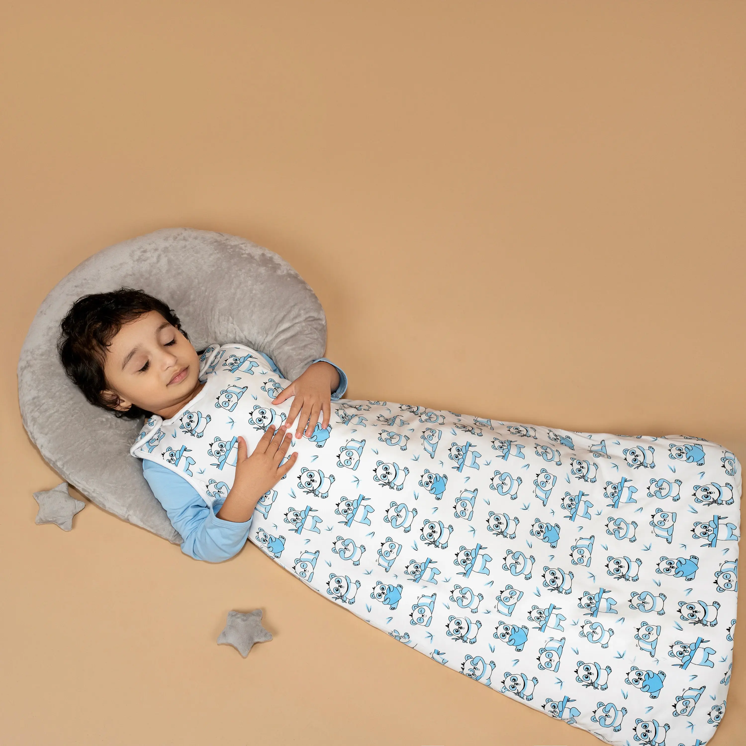 A peaceful toddler sleeping in a blue panda print sleeping bag, set against a neutral background with soft star accents.