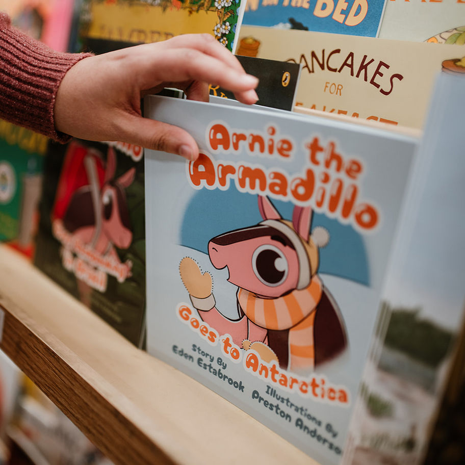 A hand grabbing a copy of Arnie the Armadillo Goes to Antarctica on a shelf