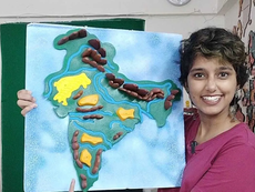 Kavya Karnatac, smiling and holding a handmade relief map of India with rivers and regions in a classroom.