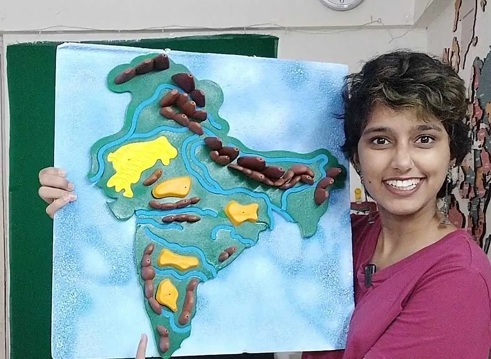Kavya Karnatac, smiling and holding a handmade relief map of India with rivers and regions in a classroom.