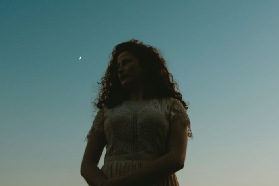 Silhouette of a woman with curly hair in a lace dress against a dusky sky with a crescent moon. Calm, introspective mood.