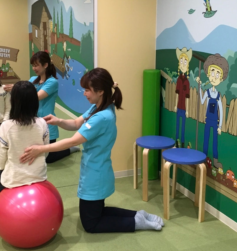 理学療法士が子供の背中を触る、セラピーの様子。壁には絵が描かれています。