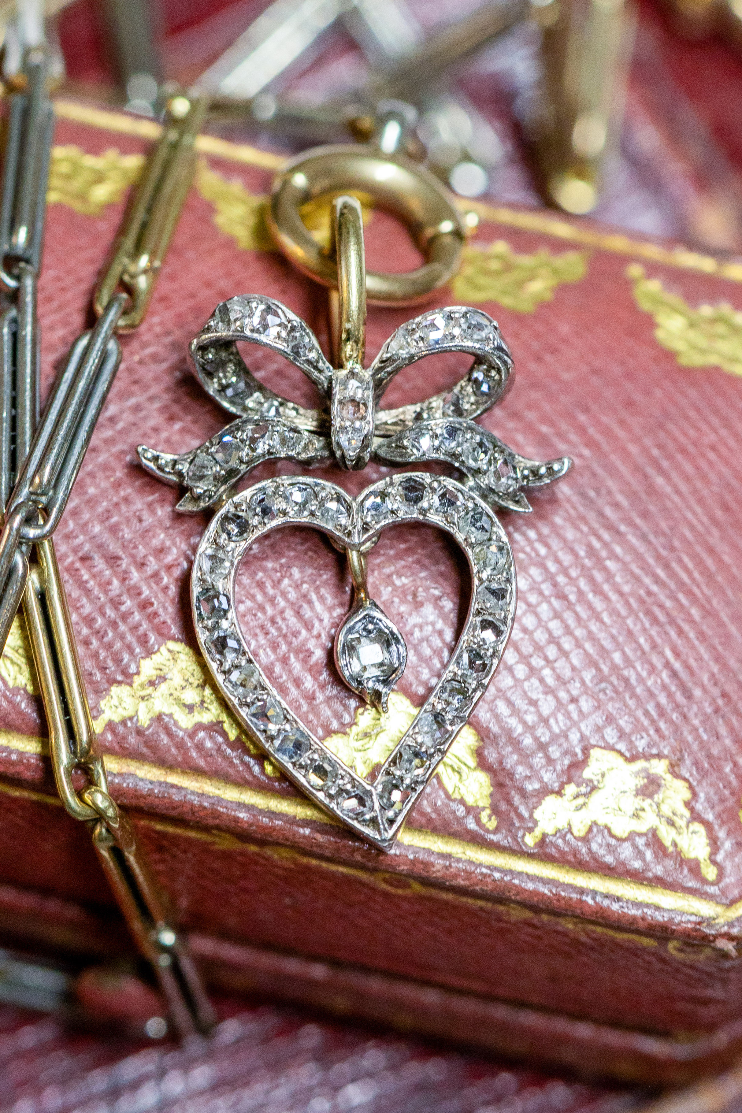 Styled flatlay of the Victorian diamond witch’s heart pendant with bow, displayed against an antique burgundy leather box.