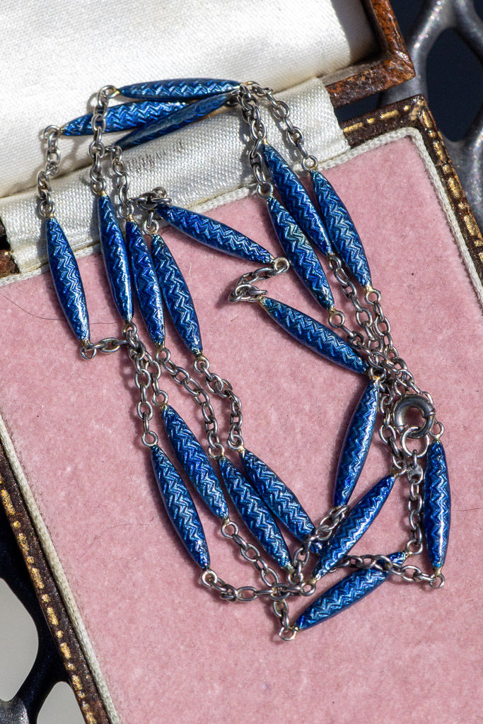 Close-up of antique platinum station chain featuring elongated cobalt blue enamel links with geometric chevron decoration.