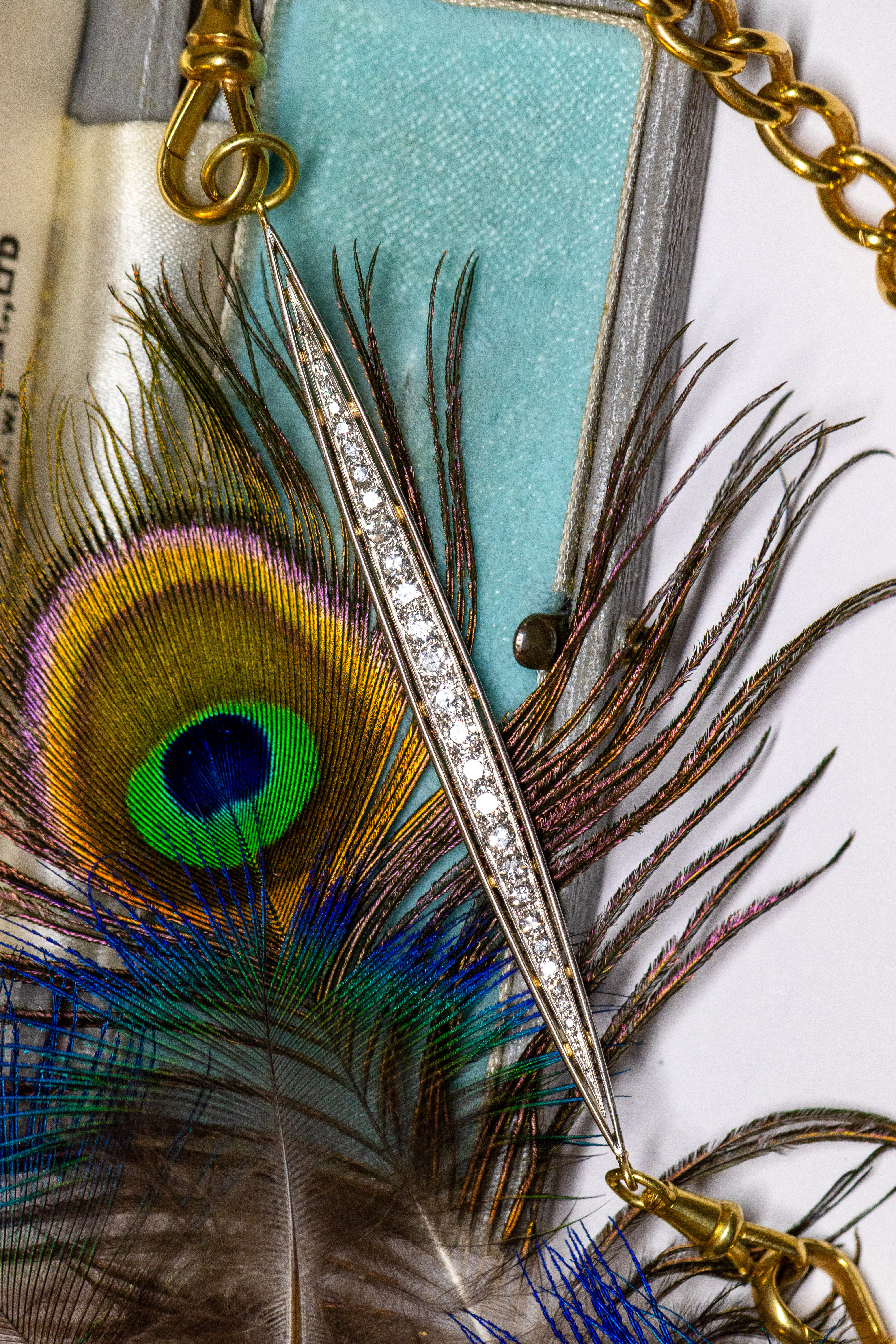 Art Deco diamond bar extender with old-cut diamonds and 18ct French swivel dog clip displayed against a peacock feather.