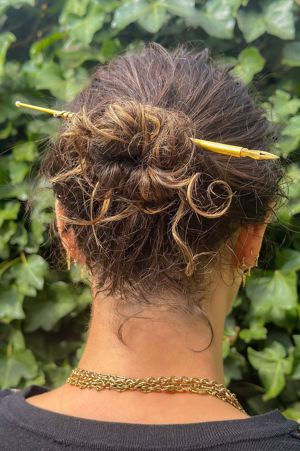 Miniatura: Gold quill pen worn as a hair pin in a model's bun, styled with soft curls and gold jewellery.