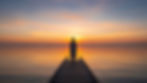 Pessoa de costas observando o nascer do sol sobre o mar calmo em um pier de madeira, representando a filosofia japonesa do ikigai, propósito de vida e reflexão sobre razão de viver.