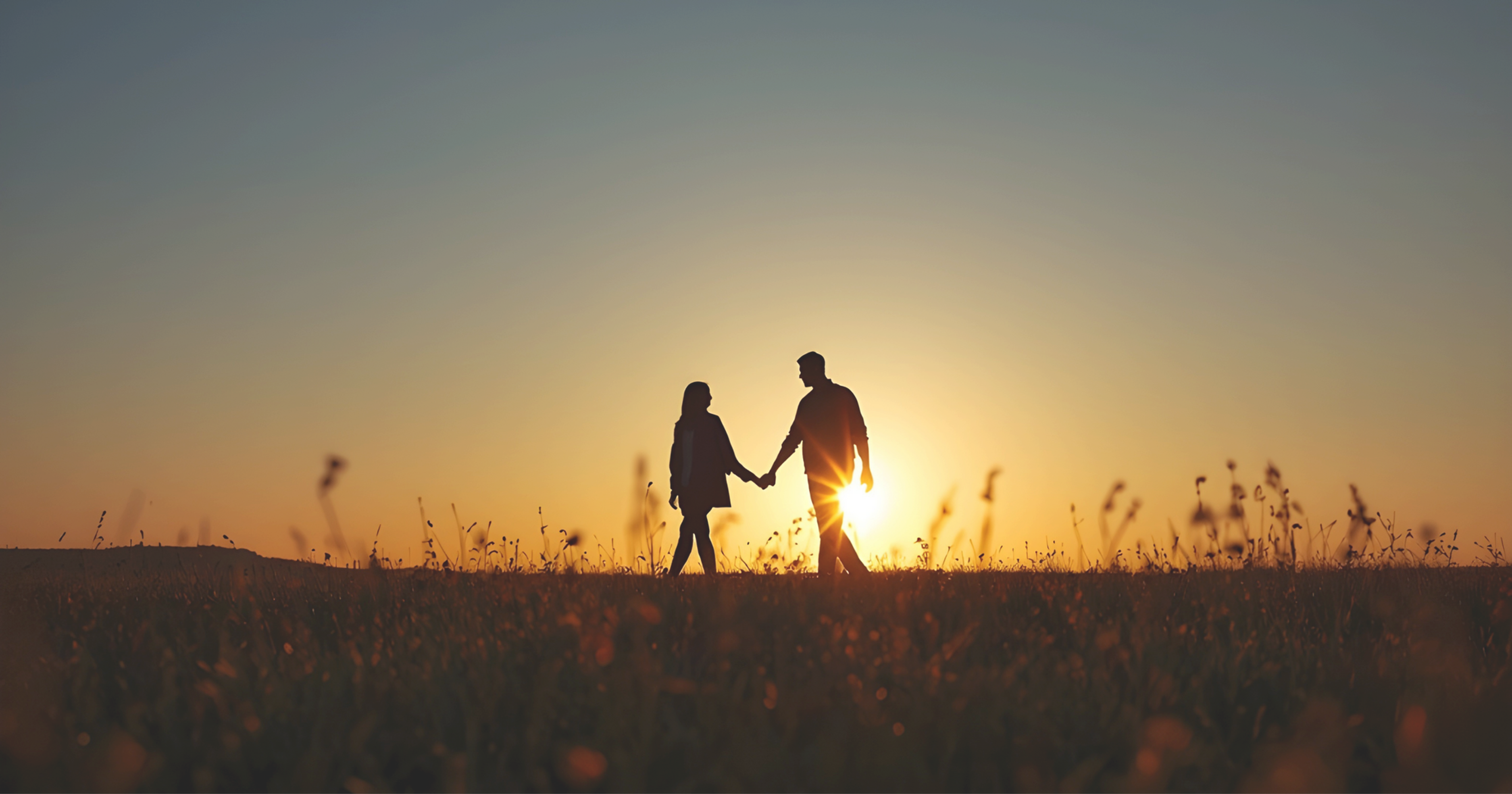 Una foto de una pareja caminando en un prado mientras el sol se pone detrás de ellos.