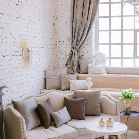 Cozy living room with couch, pillows, window, and DRAPERY. The Wallpaper Company.