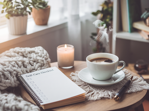 Cozy setup with a steaming coffee cup, lit candle, self-care checklist, and pen on a wooden table. Plants and books in the soft-lit background.
