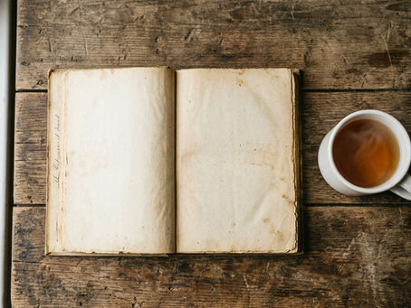 Open book and cup of tea on a wooden table in natural morning light