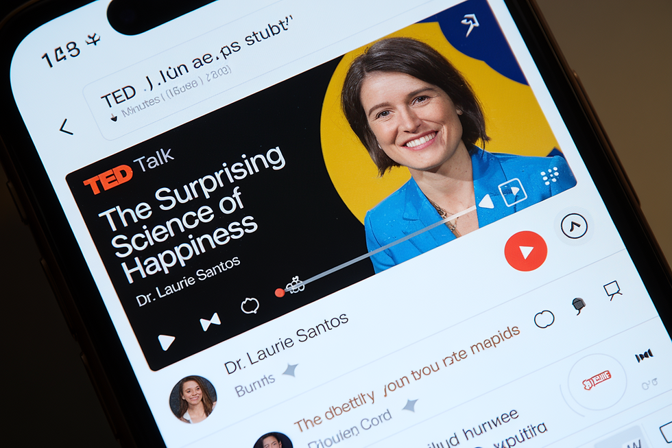 TED Talk on phone screen titled "The Surprising Science of Happiness" by Dr. Laurie Santos. Smiling woman, blue outfit, yellow-blue backdrop.