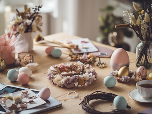 Easter-themed table with decorated eggs, floral wreaths, and a cup of tea. Soft colours and natural light create a cosy atmosphere.