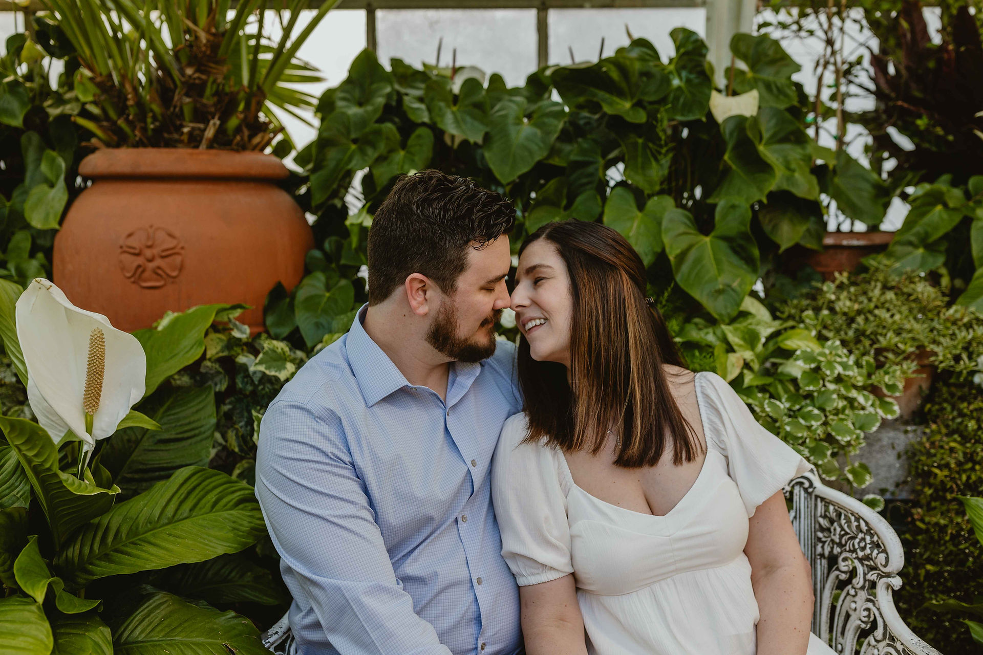 Couple is inside the conservatory sitting down on a bench. They are about to kiss the conservatory is on the Biltmore grounds. 