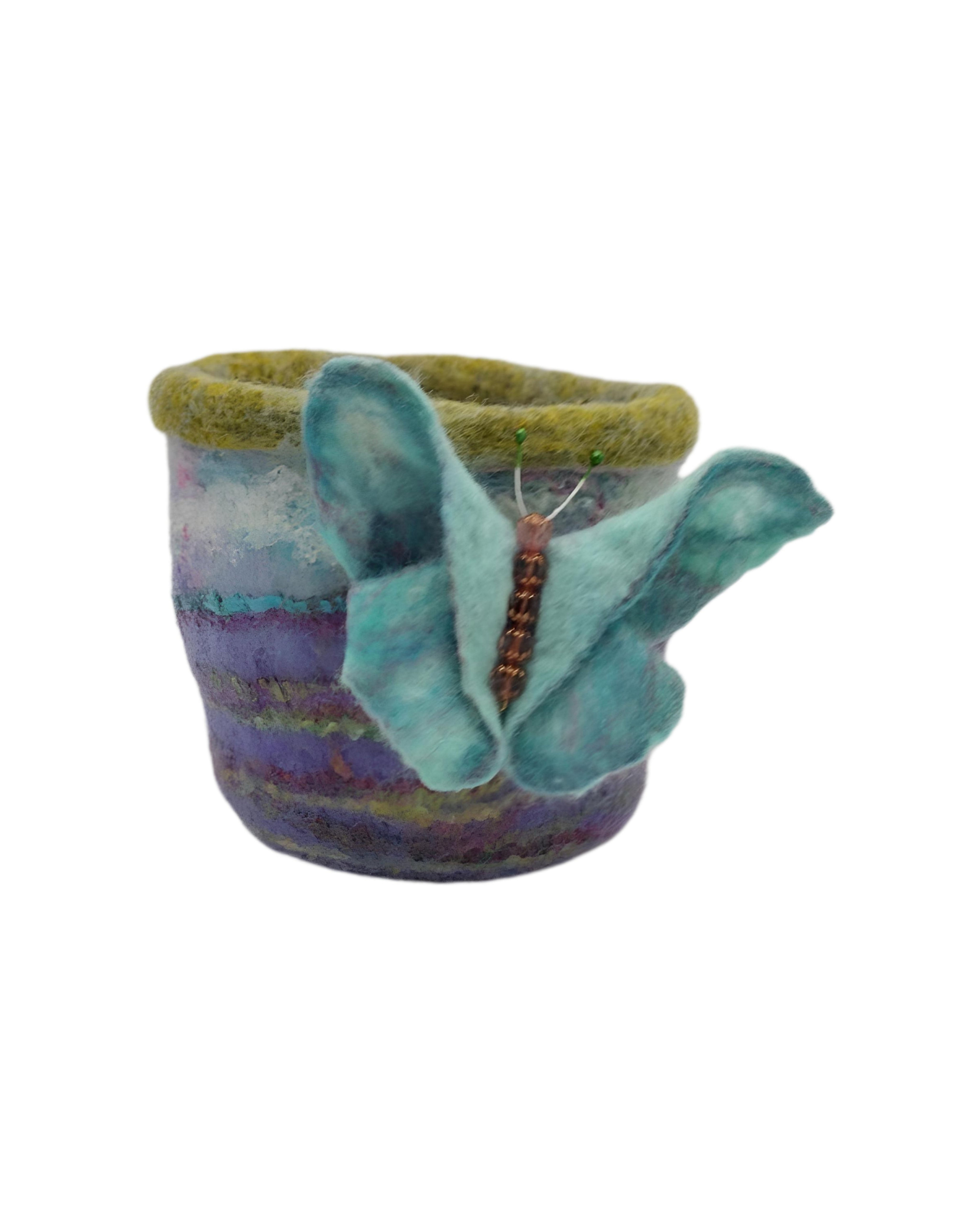 Teal coloured wool butterfly brooch resting on a felt pot