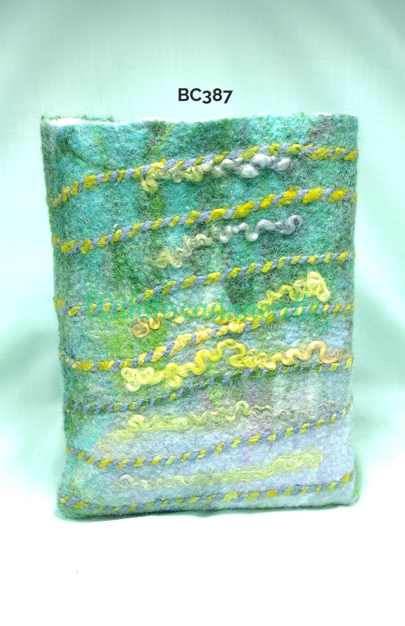 Front of a wool felt book cover dust jacket in shades of green throught to gold