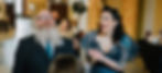 A wedding couple are laughing - the top of Linda's head is just visible and she is conducting the ceremony. The bride is wearing a beautiful gothic blue dress, the groom has a big beard.