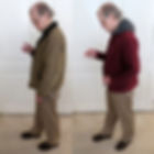 Two images of a man in tan pants: left wearing a brown coat, right wearing a red coat with gray collar. Both hold a compass, indoors.