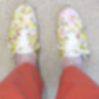 Feet in white floral sneakers and orange pants on a beige carpet, top-down view.
