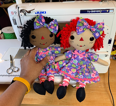 Two Raggedy Ann Dolls sitting in front of sewing machine