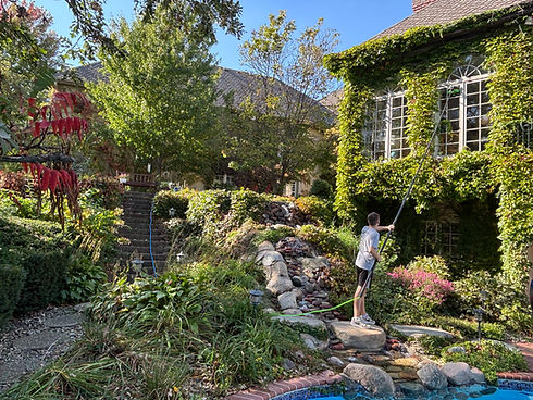 Person cleans windows near ivy-covered house next to pool
