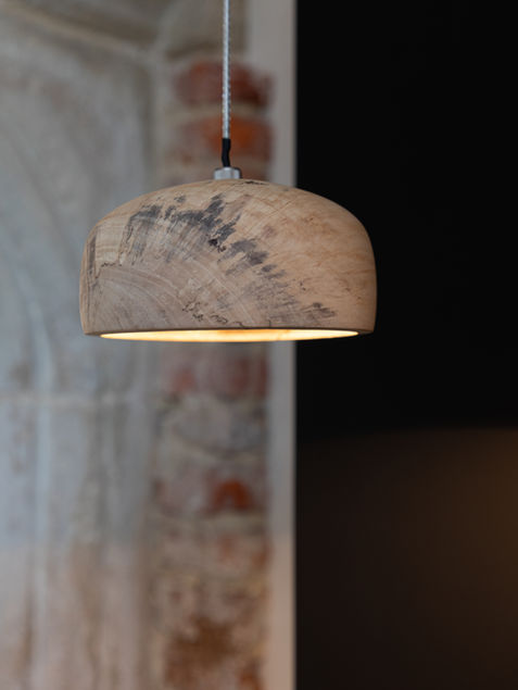 Handgemaakte houten hanglamp met gemarmerd hout tegen een oude stenen muur