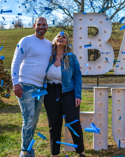 Candid capture of mother Summer and father laughing and smiling amidst blue confetti at their gender reveal