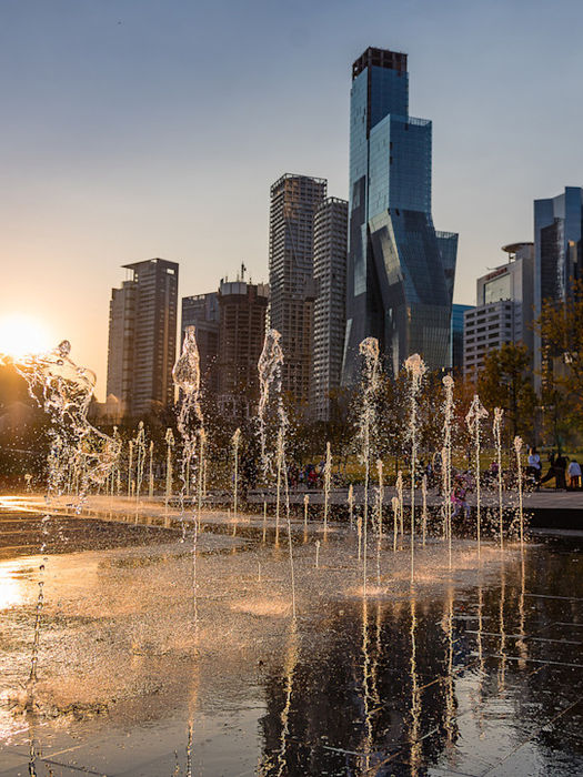 Fuente y plaza pública en Santa Fe, Ciudad de México, al atardecer, con rascacielos y edificios modernos al fondo.