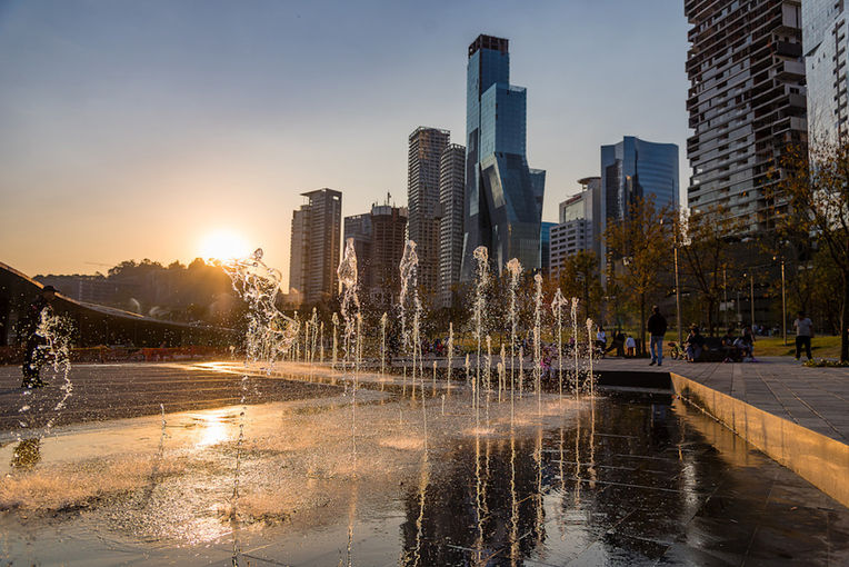 Fuente y plaza pública en Santa Fe, Ciudad de México, al atardecer, con rascacielos y edificios modernos al fondo.