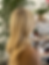 A women standing in a bright salon environment, with blonde hair beautifully styled after a balayage service with sunkissed, natural, bright highlights