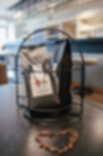 Zwei Tüten Haus Karlich Röstkaffee stehen in einem Drahtkorb, mit einem Herz aus Kaffeebohnen im Vordergrund. Die Tüten haben