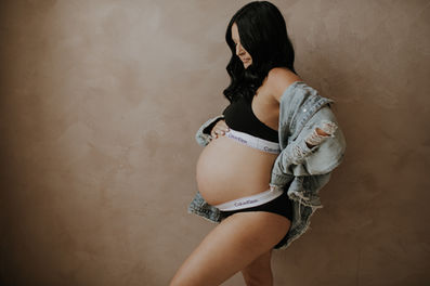 a pregnant woman wearing a jean jacket and bra holding her baby bump with her hand on her hip