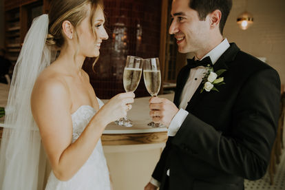 A bride and groom holding champagne glasses cheers-ing each other