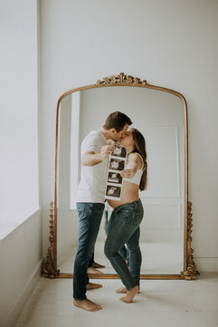 a husband and wife kissing while holding ultrasound photos for their concord maternity photoshoot
