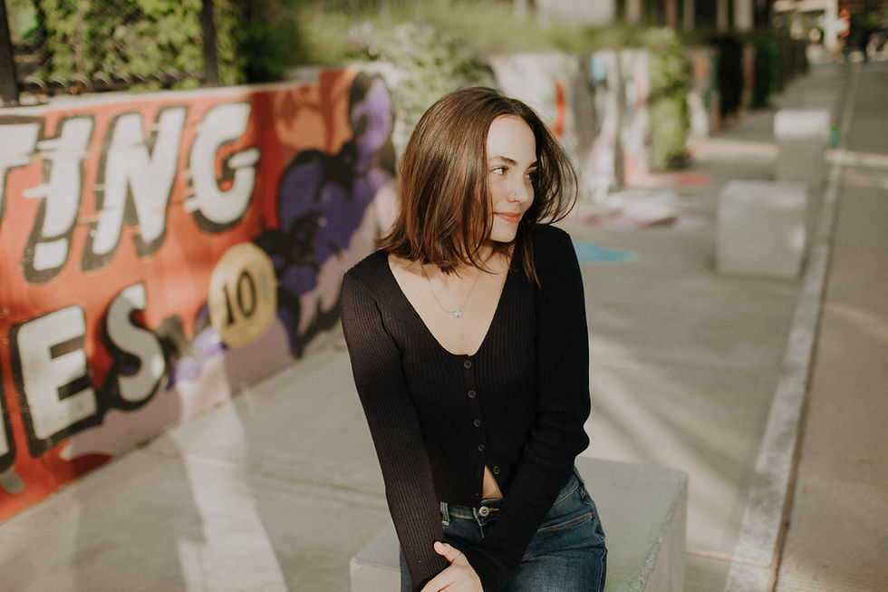 a high school senior girl in a blue sweater in front of a graffitied wall smiling off to the side for her Charlotte senior portraits
