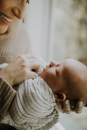 a mom holding a baby boy very close near a window for her candid newborn photographer in Charlotte