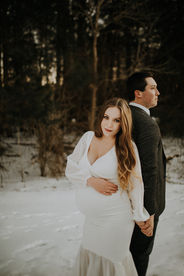 a pregnant woman holding her belly looking at the camera in a white dress holding her husband's hand during her davidson maternity session