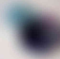 Zbliżenie na dwuelementową pracę ceramiczną Lidii Misiuny ustawioną na białym postumencie: na pierwszym planie widoczna jest połyskująca, owalna „skorupa” otwarta z przodu, w barwach głębokiego granatu i fioletu; brzegi są zaokrąglone, a w środku widać lśniącą, ciemnoniebieską powierzchnię z wyraźnymi, falistymi żłobieniami. Za nią leży drugi element — gładka, wydłużona forma przypominająca kroplę, szkliwiona w turkusie z licznymi, drobnymi, złocisto‑piaskowymi nakrapianiami i wypukłościami; oba obiekty są błyszczące i kontrastują z matową bielą postumentu.