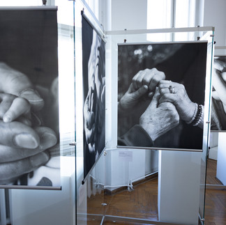 Zestaw czarno‑białych fotografii Lidii Misiuny: pierwsza pokazuje ciasno splecione dłonie wypełniające cały kadr; druga przedstawia dłonie dwóch osób stykające się w delikatnym, precyzyjnym geście; trzecia ukazuje skrzyżowane ramiona i dłonie spoczywające na ciele, widziane z bliska bez tła narracyjnego.