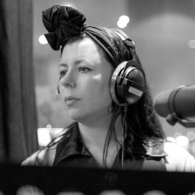 Composer Daisy Coole is pictured in a recording studio wearing headphones with a microphone visible on the right hand side of the image