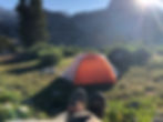 man relaxing by a tent in the mountains