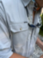 Person in a light shirt with sunglasses in pocket, colorful neck gaiter. Label reads PONCHO. Gravel and greenery in background.