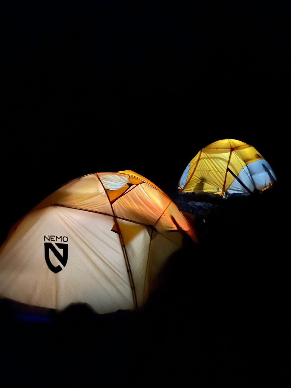 Glowing orange and yellow tents labeled "NEMO" in a dark night setting, creating a warm and peaceful camping scene.