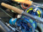 Close-up of fly fishing rods with cork handles and blue reels marked "Bauer" and "R.L. Winston Rod Co." Colorful fishing lines are visible.